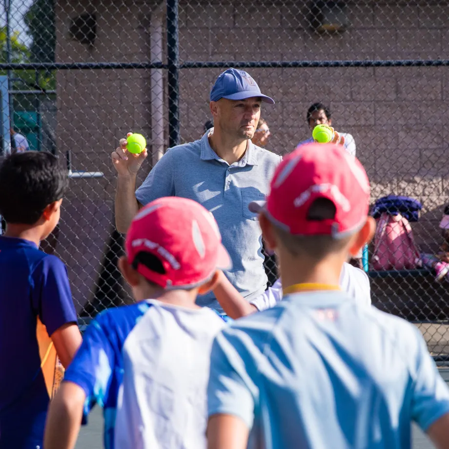 Leon Bax holding up a ball while coaching a group of young players on a tennis court