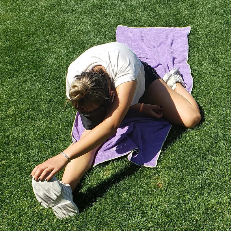 A junior player on grass in a deep seated forward fold, head down over an outstretched leg.